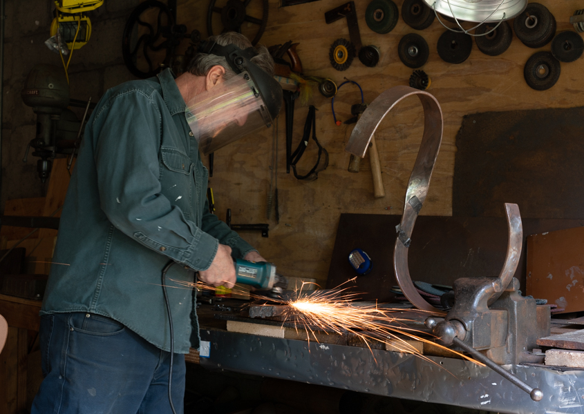 Artist Howard Lewis working on a metal piece in his workshop with sparks flying.